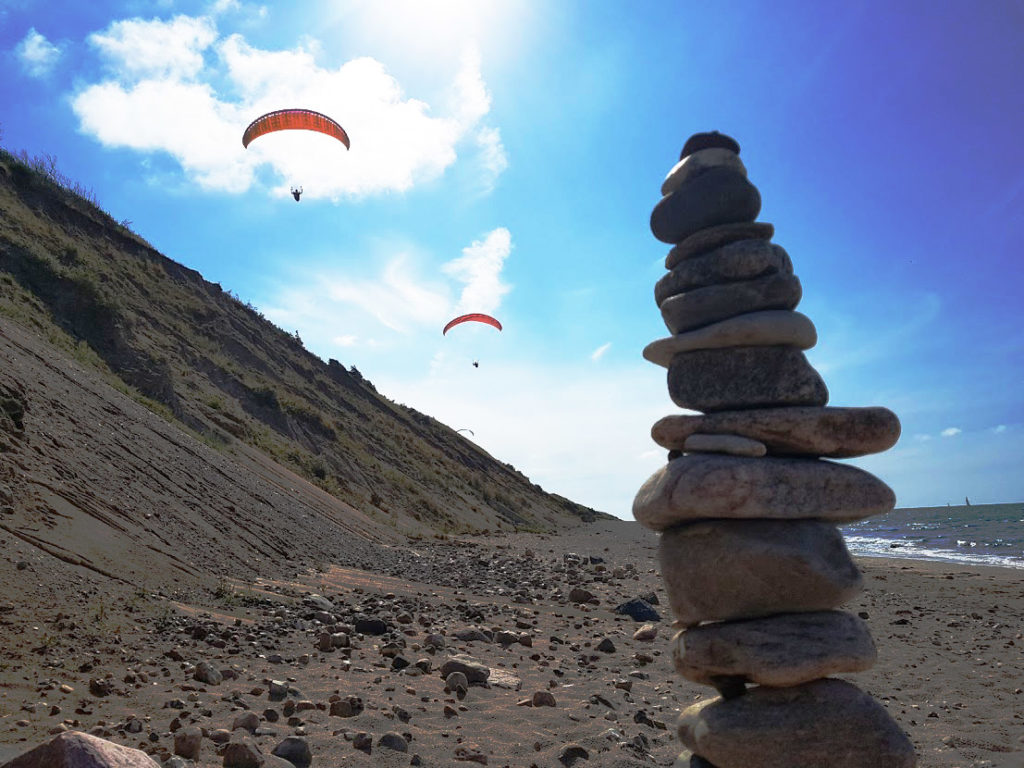 rocks balancing in a stone cairn on the beach with paragliders in the background, representing a work life balance
